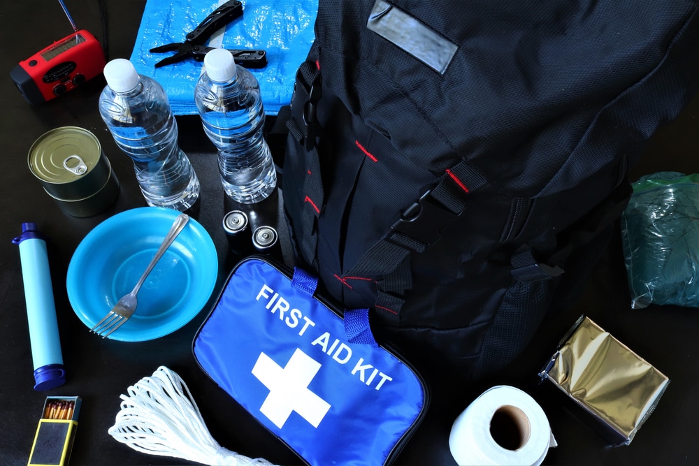 Emergency survival kit items including a black backpack, first aid kit, water bottles, and canned food