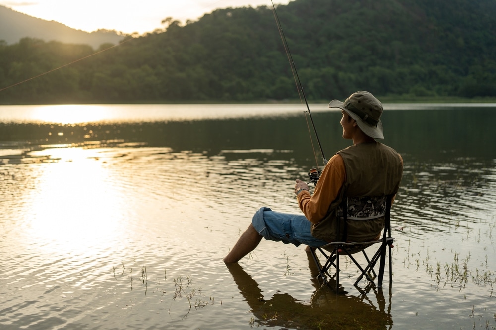 Man sitting in a folding chair fishing in a calm lake at sunset