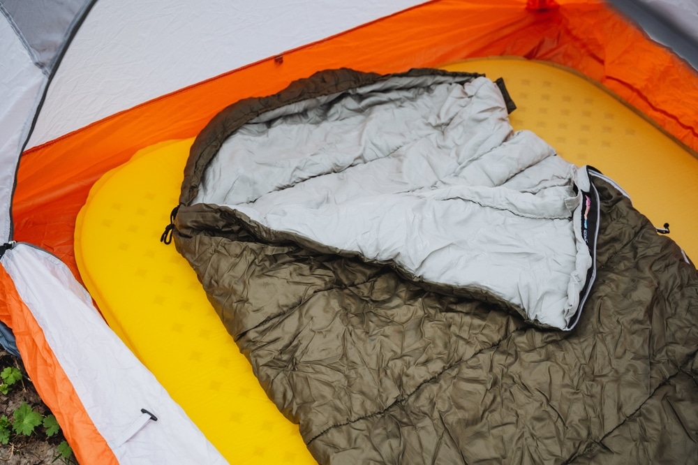 Open sleeping bag on a yellow sleeping pad inside an orange camping tent