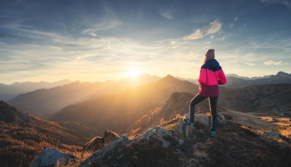 Hiker standing on a rocky mountain peak looking out over a valley at sunrise