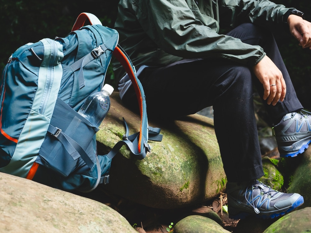 Hiker taking a break sitting on a mossy rock next to a blue backpack