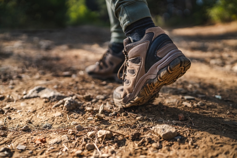 Close-up of a person walking on a rocky dirt trail wearing brown hiking boots