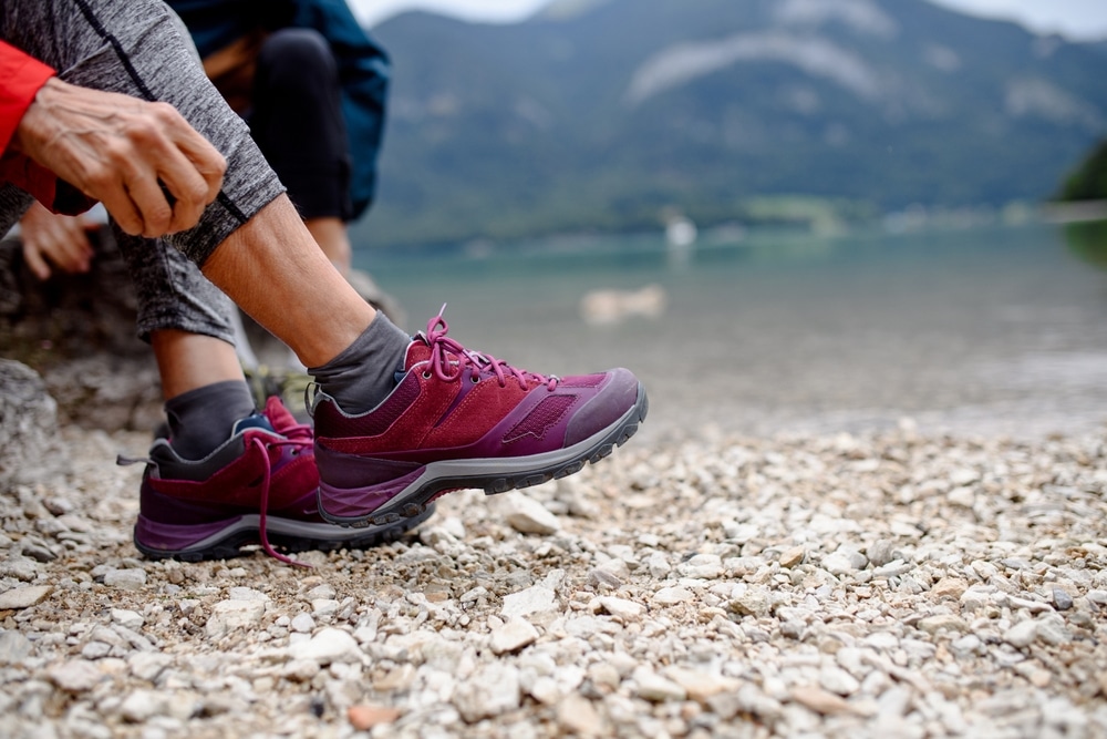 Close-up of a hiker sitting on a pebbled beach wearing purple trail shoes