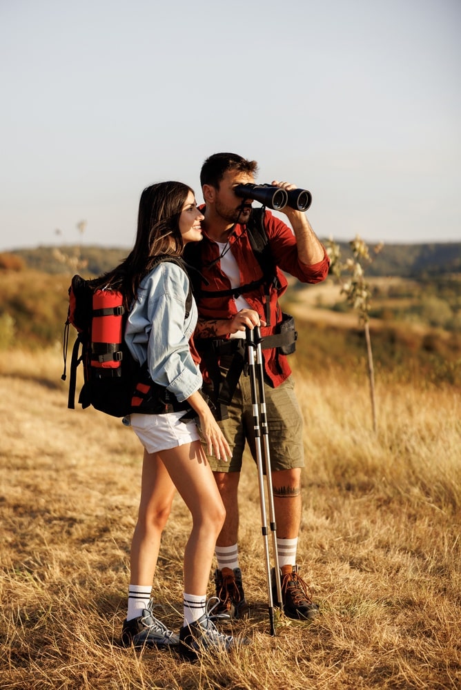 Couple hiking in a grassy field with the man looking through binoculars